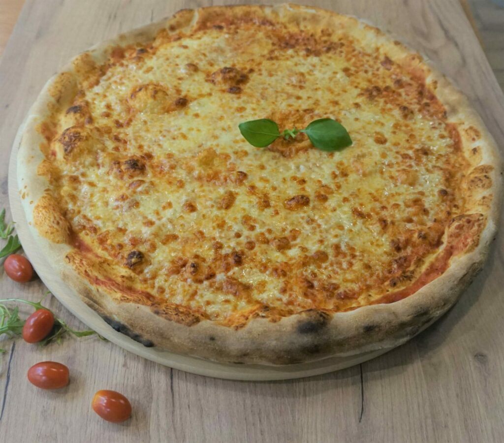 Cała, serowa pizza z sosem pomidorowym i listkami bazylii na drewnianej desce i blacie - margherita.